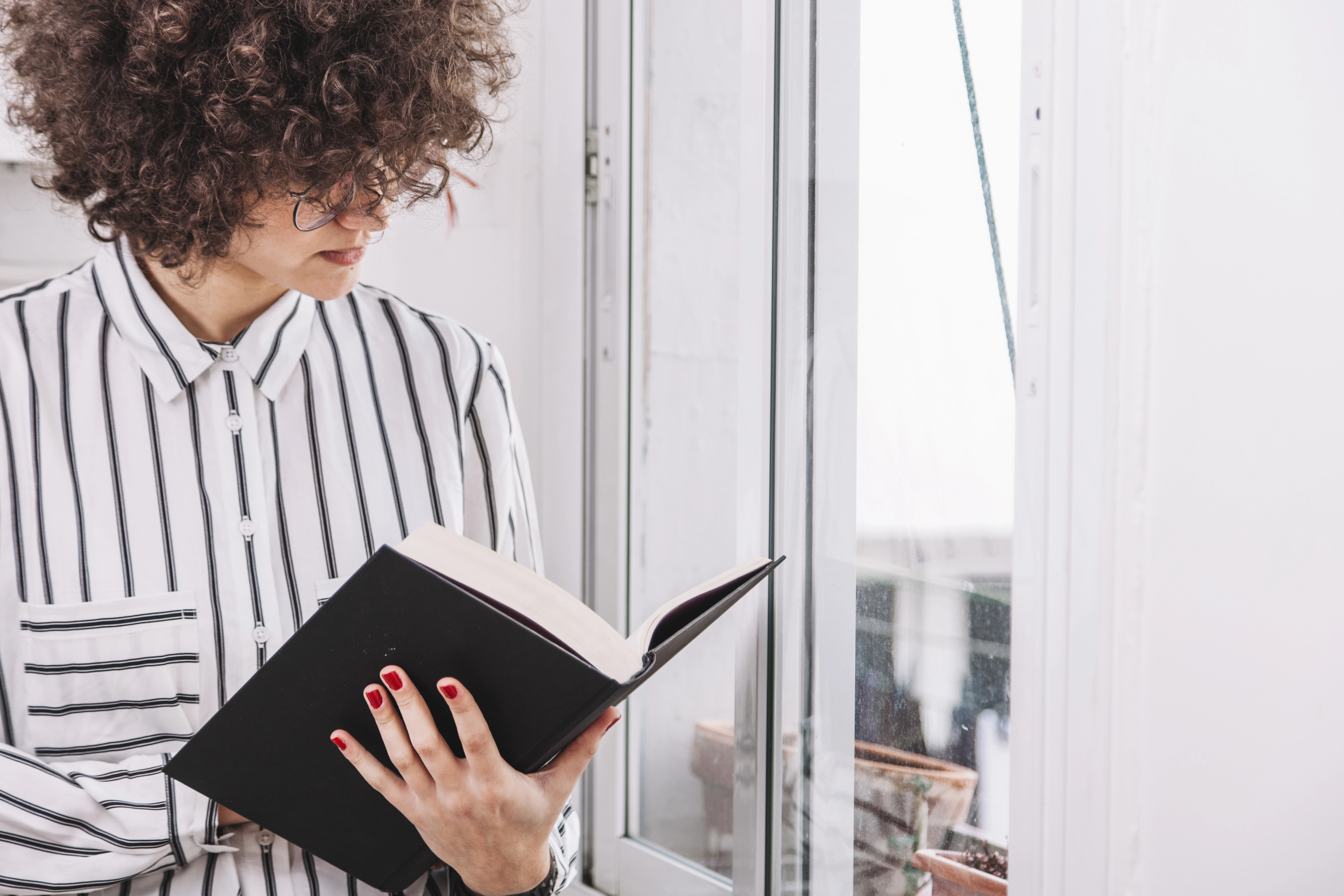 Agente literario leyendo libro junto a ventana.