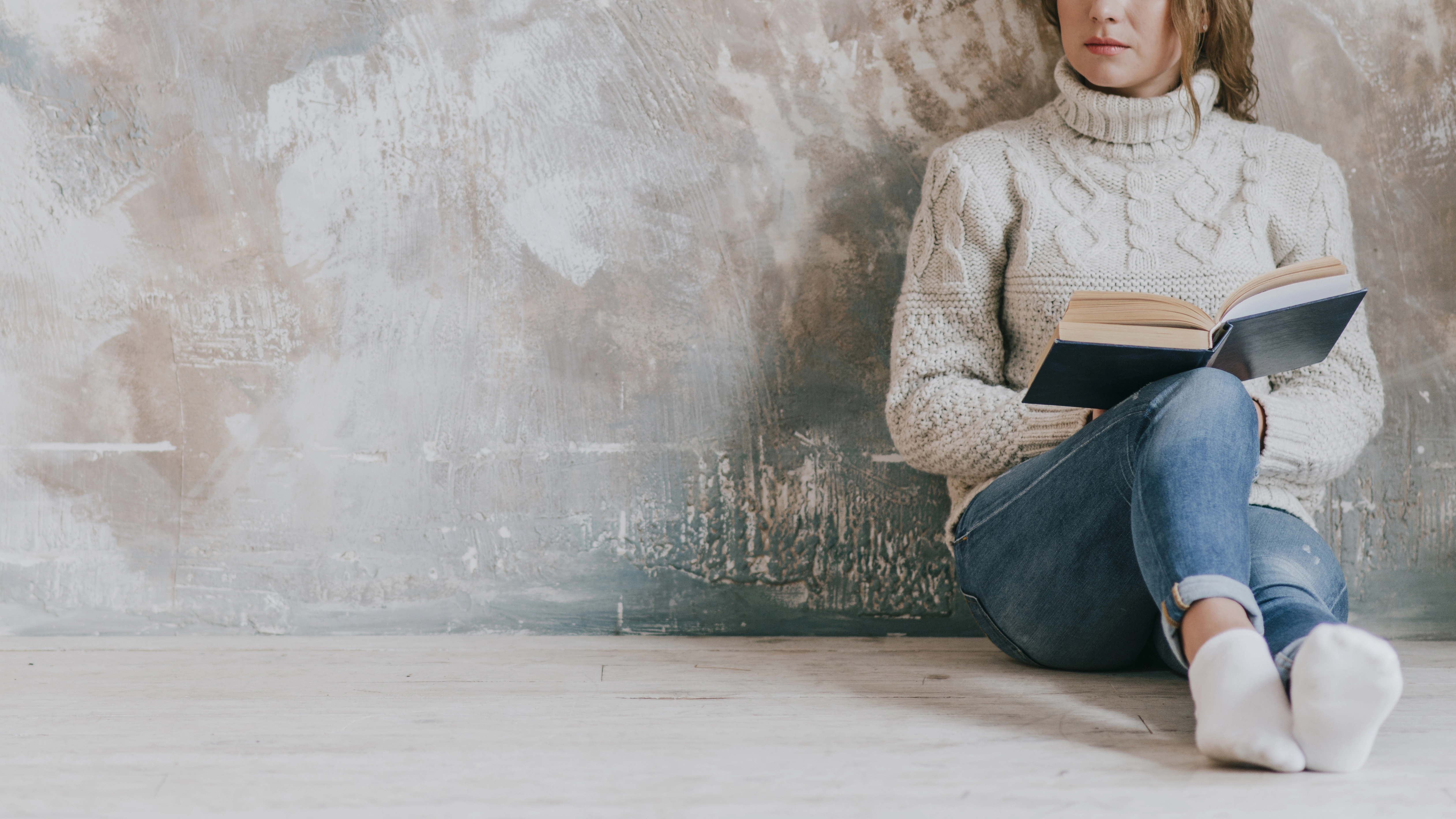 Mujer sentada contra la pared leyendo libro de antagonista.