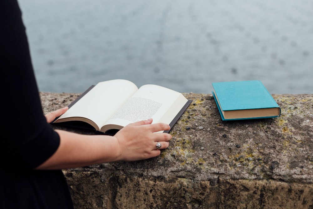 Mujer con libro abierto en cliffhanger y mar de fondo. 